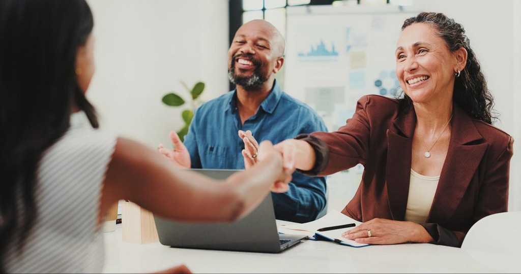 Profissionais em entrevista de emprego apertando as mãos em escritório corporativo, representando estratégias de gestão de talentos e recrutamento empresarial.